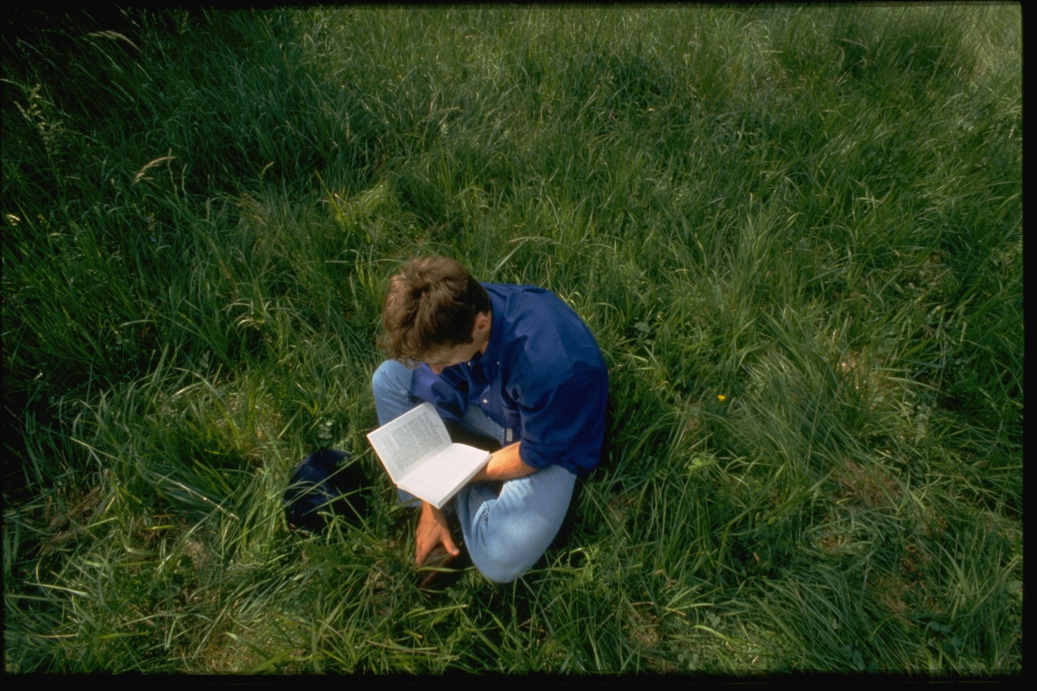 A man sitting on grass and reading a book.