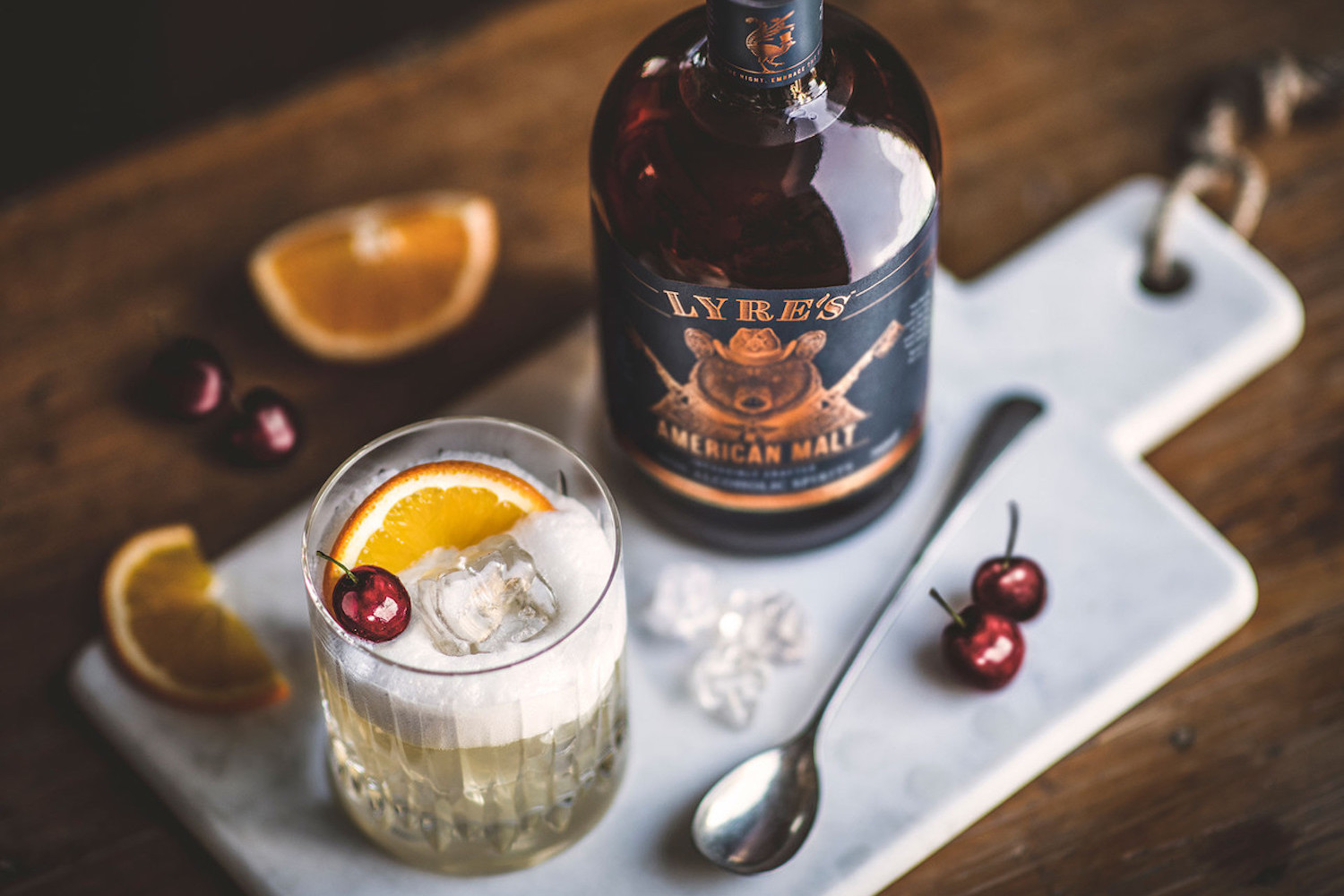 lyre's american malt bottle and sour cocktail on a white marble board