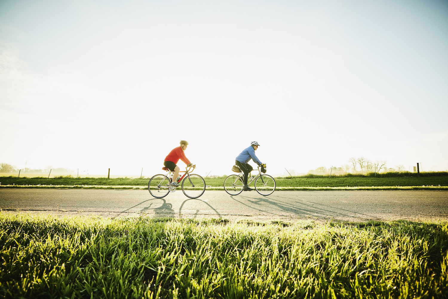 Wide shot of senior male friends on sunrise bike ride on rural road