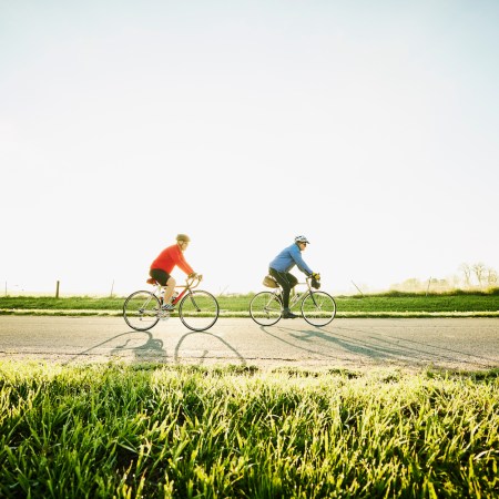 Wide shot of senior male friends on sunrise bike ride on rural road