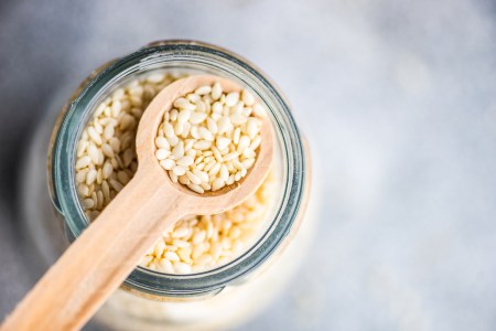 Overhead view of a glass jar of sesame seeds with a wooden spoon