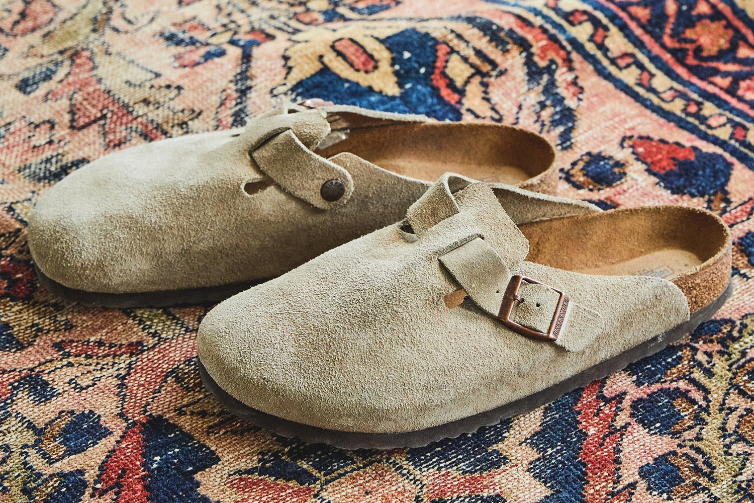 a pair of beige Birkenstock Boston slides on a carpeted background