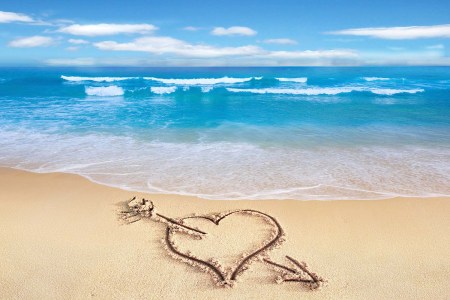 A heart drawn in the sand on a beach with waves in the background. This might be the year of the Valentine's Day trip.
