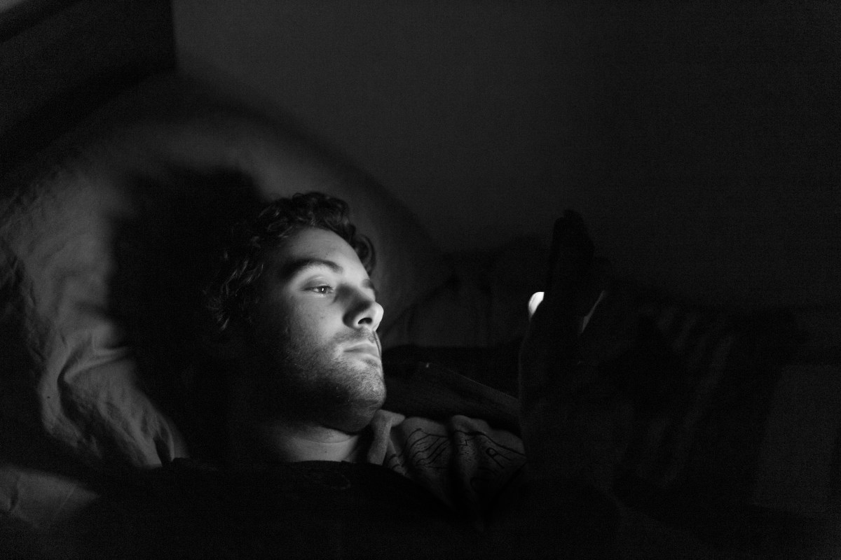 A black and white photo of a man looking at his phone in bed.