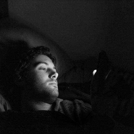 A black and white photo of a man looking at his phone in bed.