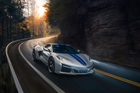 The 2024 Chevrolet Corvette E-Ray 3LZ convertible in Silver Flare with Electric Blue stripe package driving on a curved mountain road