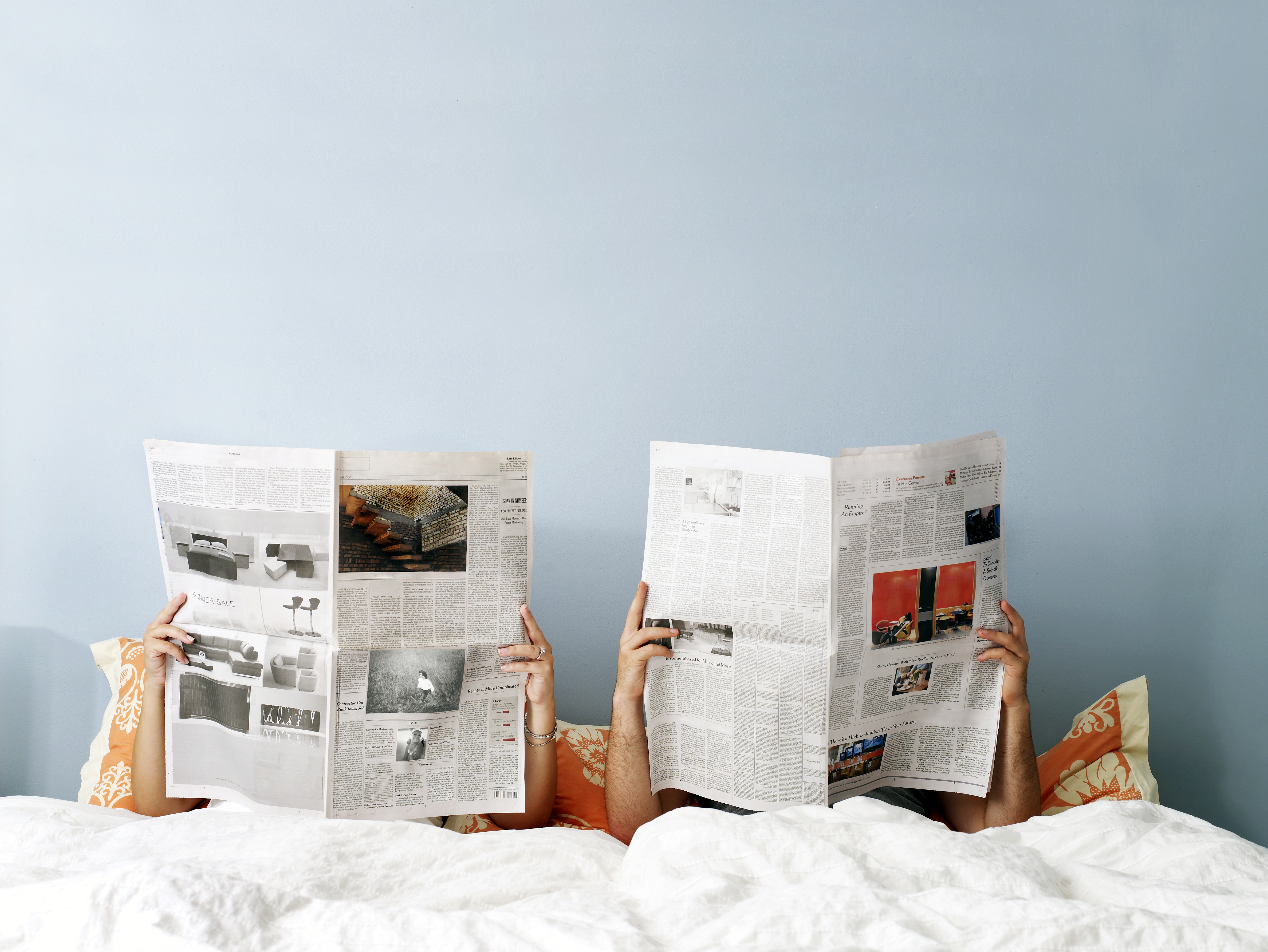 A couple reading the newspaper in bed.