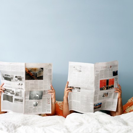 A couple reading the newspaper in bed.