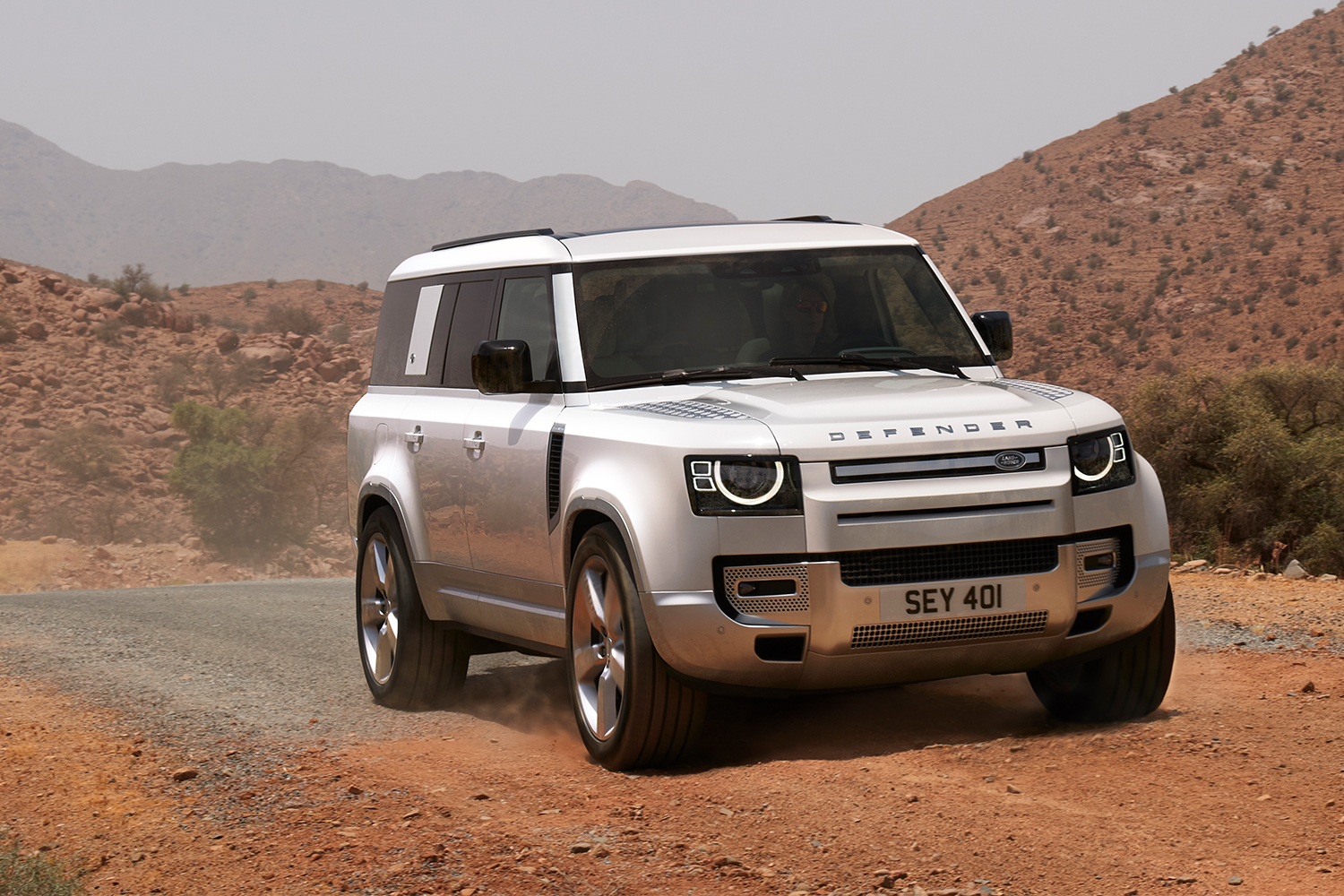 The Land Rover Defender 130, the three-row version of the SUV, in white driving down a sandy road