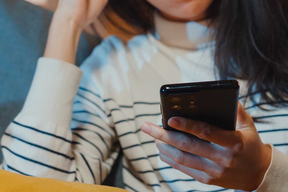 A woman holding a phone sitting on a couch. A non-profit mental health service recently admitted to using an AI-powered chatbot to assist its human operators in sessions without user knowledge