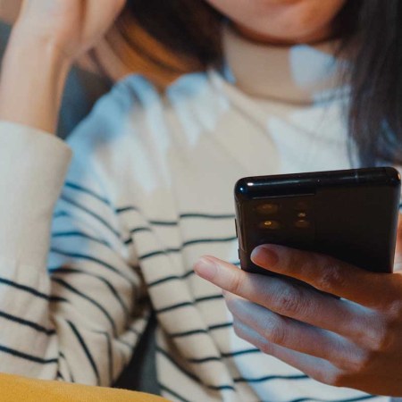 A woman holding a phone sitting on a couch. A non-profit mental health service recently admitted to using an AI-powered chatbot to assist its human operators in sessions without user knowledge