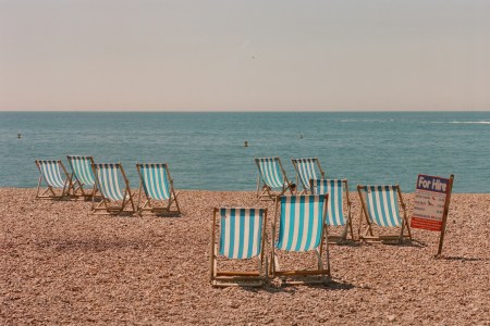 A scattering of empty pinstriped beach chairs on a rocky shoreline.