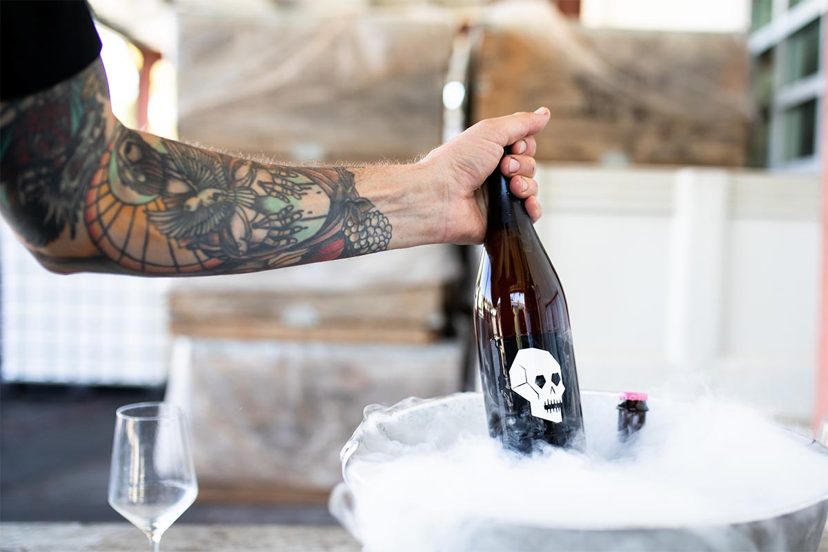An arm pulling up a bottle of Skull Piquette from a bucket of ice