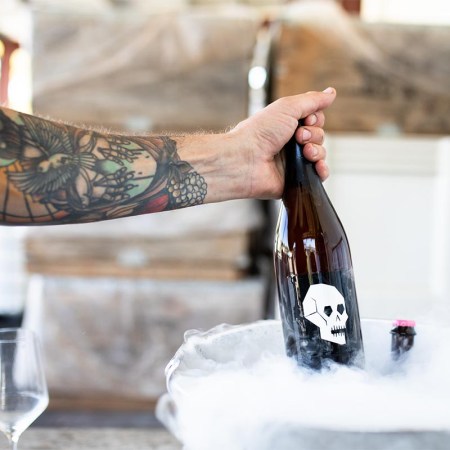 An arm pulling up a bottle of Skull Piquette from a bucket of ice