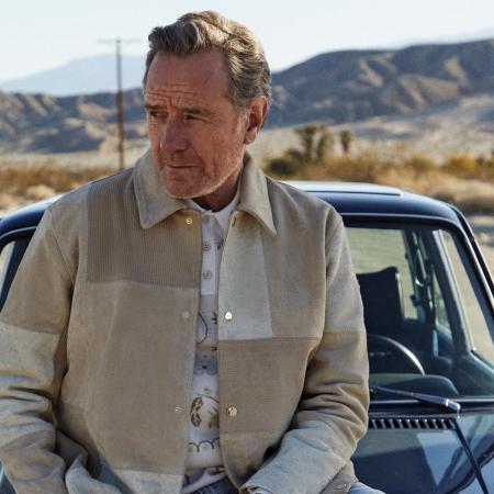 a photo of Bryan Cranston in Kith clothing siitting on a vintage car in the desert