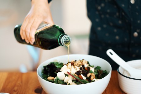 A person pouring olive oil into a salad with mozzarella, mixed nuts and dry fruits. Olive oil is projected to get more expensive in 2023 due to a poor European harvest in 2022.