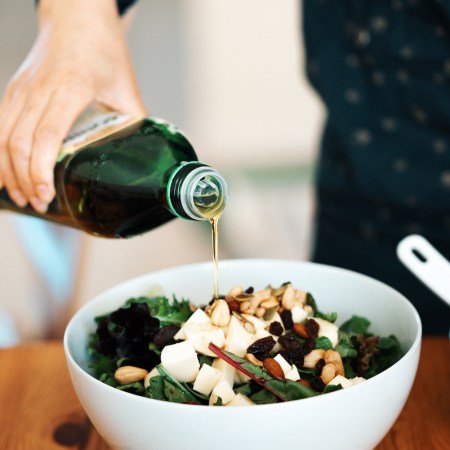 A person pouring olive oil into a salad with mozzarella, mixed nuts and dry fruits. Olive oil is projected to get more expensive in 2023 due to a poor European harvest in 2022.