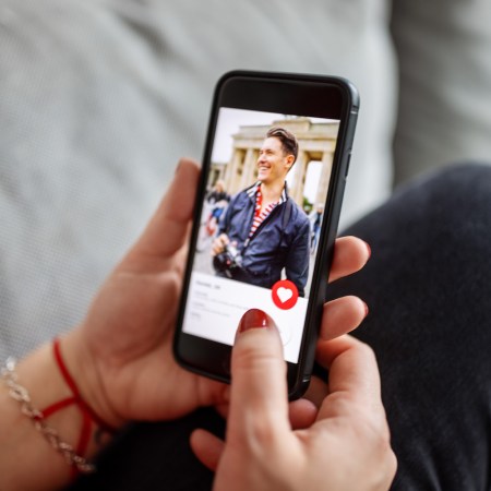 Woman with red nails looking at man on an online dating app on her mobile phone