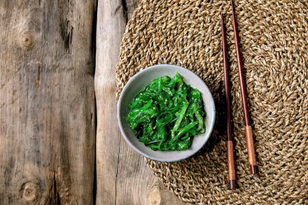 Japanese Wakame chuka seaweed salad with sesame seeds in ceramic plate with chopsticks over old wooden background