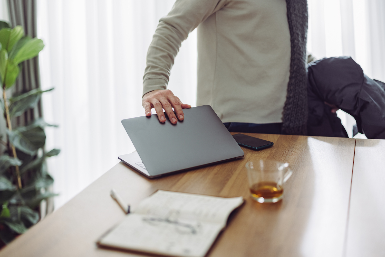 An Anonymous Businessman closing his laptop that's sitting on a wooden table next to a glass of whiskey