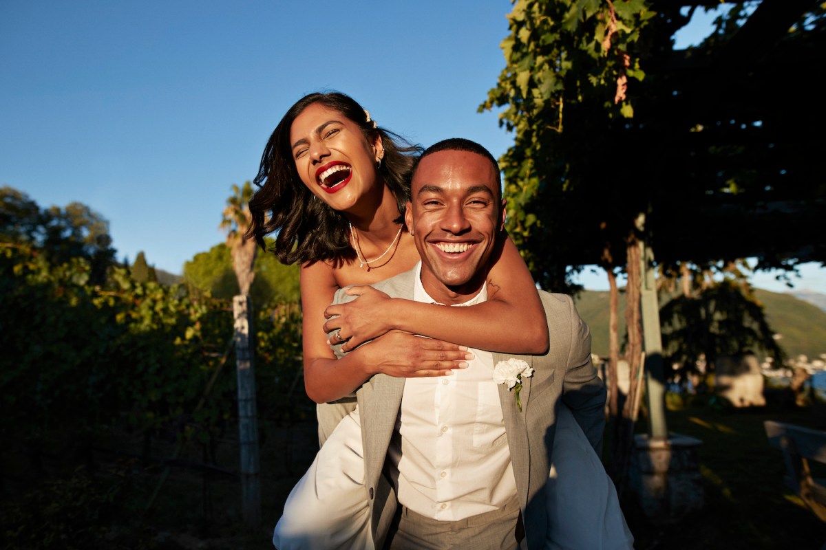 Happy groom piggybacking bride in vineyard during sunset