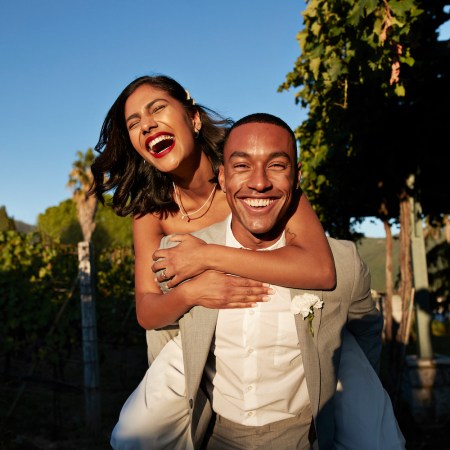 Happy groom piggybacking bride in vineyard during sunset