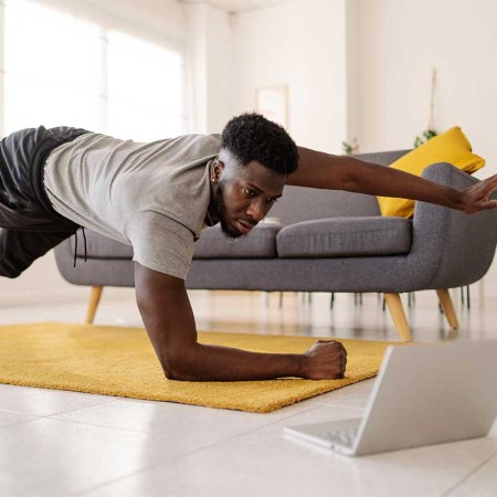 Man watching online exercise video on laptop while working out in the living room at home. ChatGPT is being used by some exercise hobbyists to create workout plans.