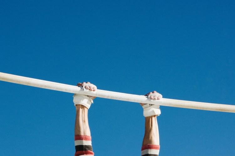 A pair of hands clutching a gymnastics beam. Grip strength may be related to living longer, according to some studies.