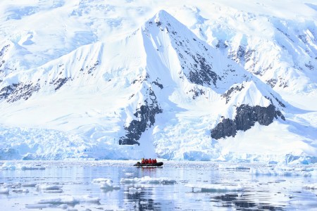 A Zodiac boat from travel company Abercrombie & Kent ferrying travelers past mountains and icebergs during an Antarctica cruise
