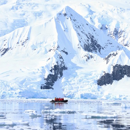 A Zodiac boat from travel company Abercrombie & Kent ferrying travelers past mountains and icebergs during an Antarctica cruise