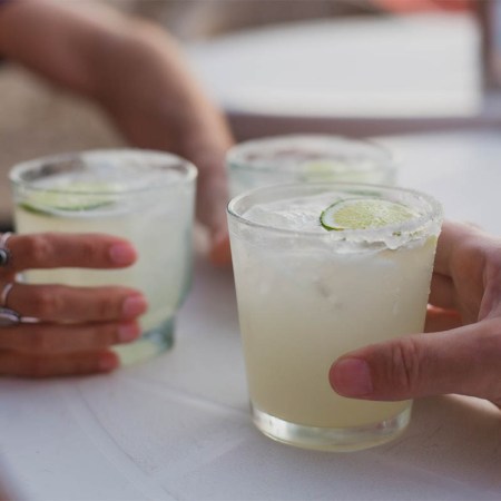 Three people (hands only) holding three full margaritas on a table. According to a new economic report by DISCUS, spirits sales (helped by tequila) just passed beer sales in the U.S.
