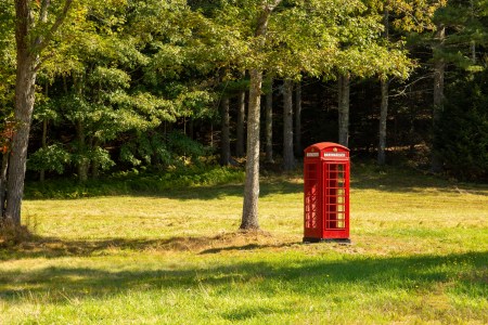 A red telephone booth in a meadow.