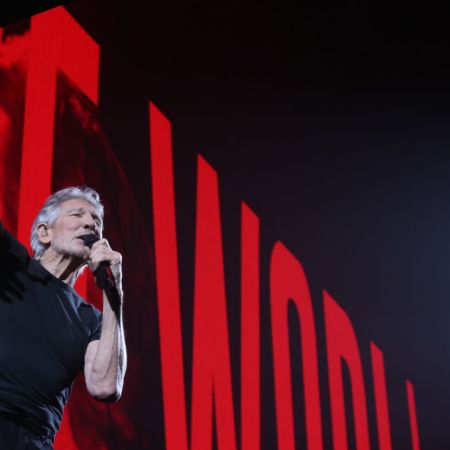 Roger Waters performing in front of a red sign