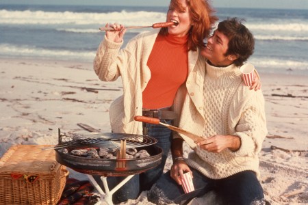 A couple eating hot dogs outside on the beach.
