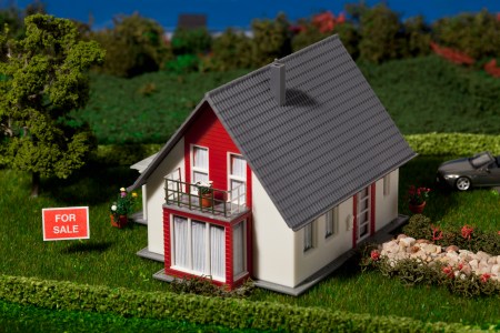 A diorama of a suburban home with a For Sale sign.