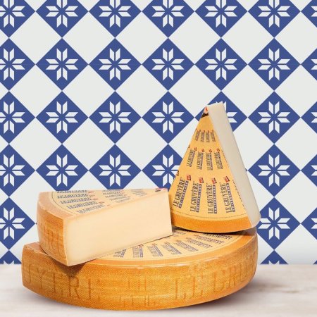 a wheel of gruyere cheese with two wedges on top of it sitting in front of a blue and white tiled wall