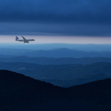 Commercial airplane flying above mountain ranges in cloudy sky at night.