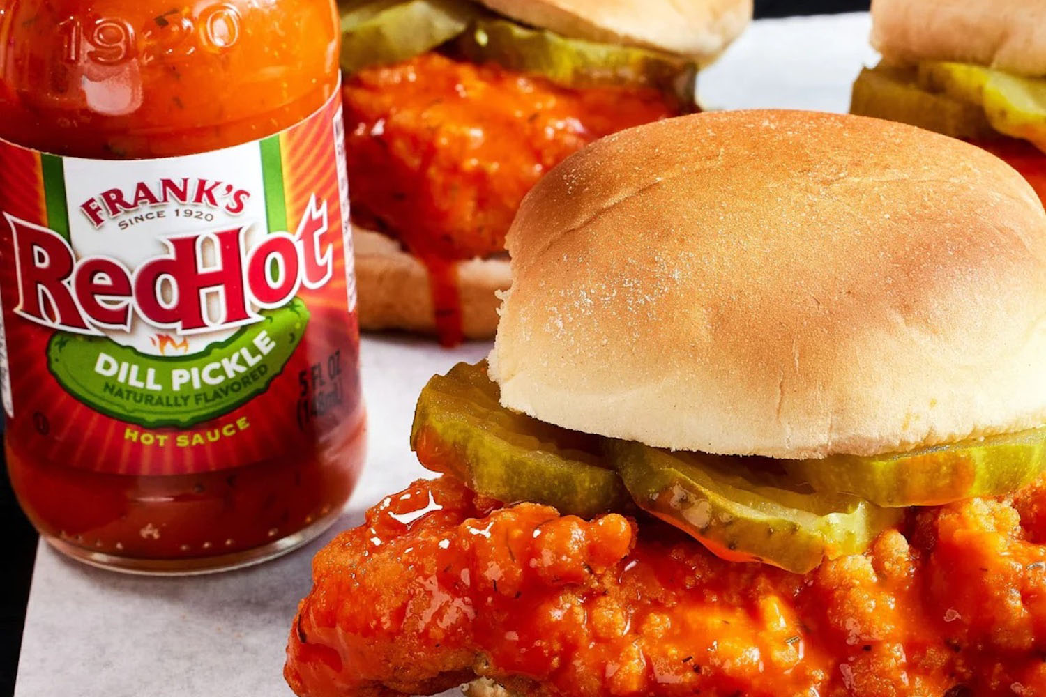 a bottle of Frank's RedHot Dill Pickle Hot Sauce next to a chicken sandwhich