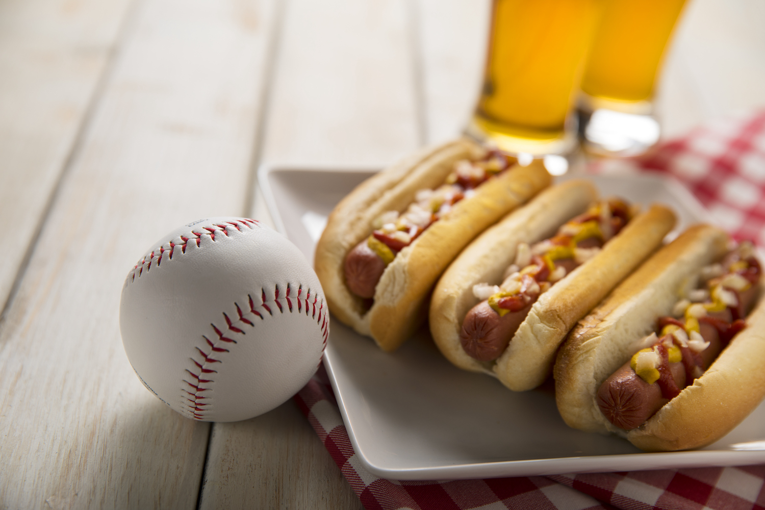 Three hot dogs on a white plate on a white wooden picnic bench
