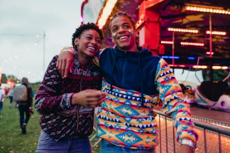 Gen z couple laughing and talking as they walk around a funfair