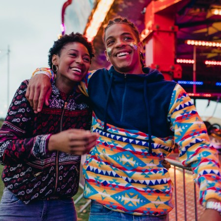 Gen z couple laughing and talking as they walk around a funfair