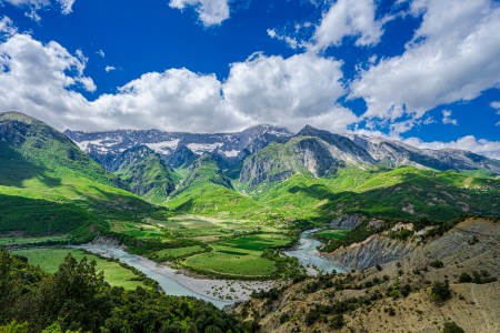 Vjosa river valley albania and the snow capped mountains beyond it under a cloud-blue sky on a sunny day from aan elevated position above the valley