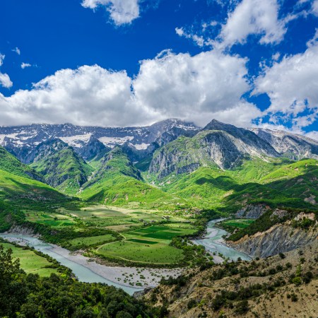 Vjosa river valley albania and the snow capped mountains beyond it under a cloud-blue sky on a sunny day from aan elevated position above the valley