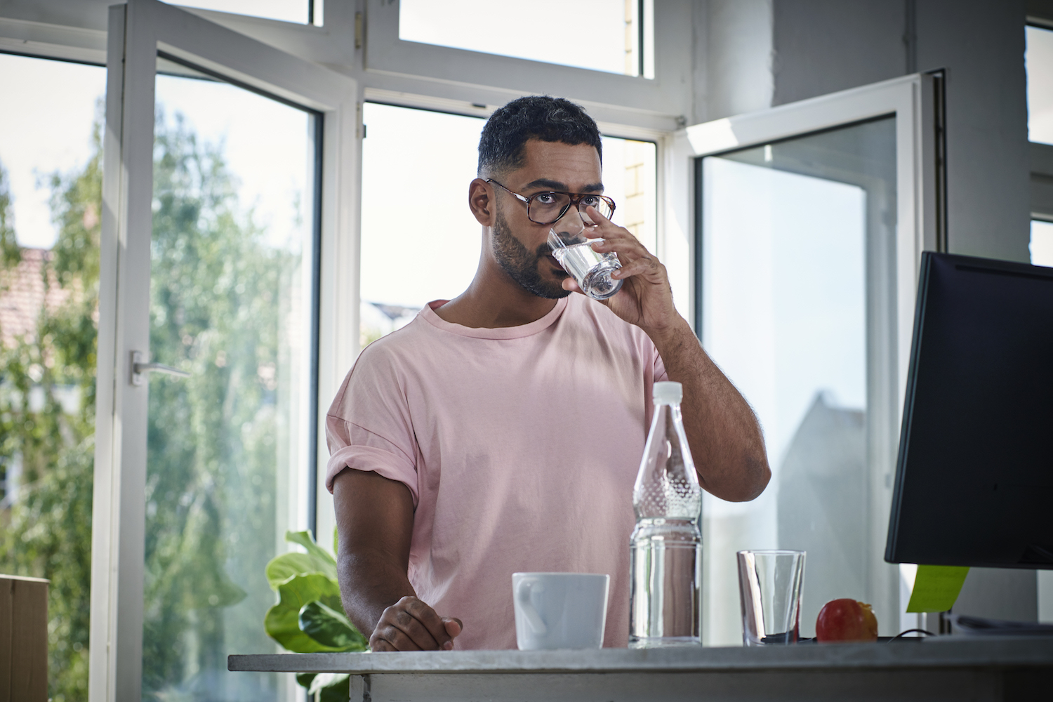 man in a pink tee shirt and glasses drinking water