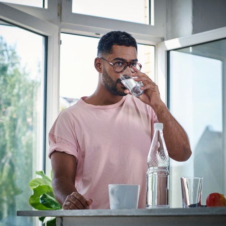 man in a pink tee shirt and glasses drinking water