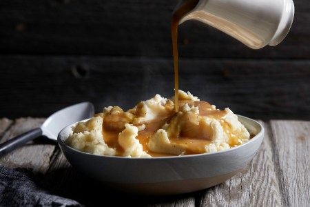 Jug of gravy being poured onto bowl of steaming mashed potatoes