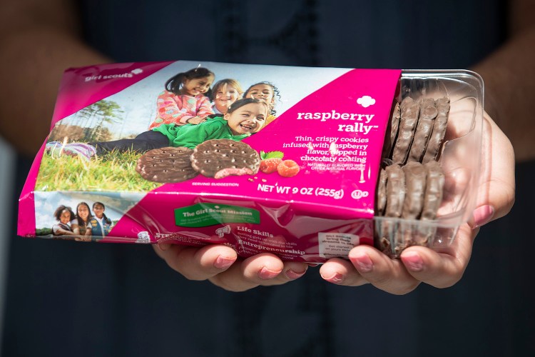 a girl scout holding a box of Raspberry Rally cookies