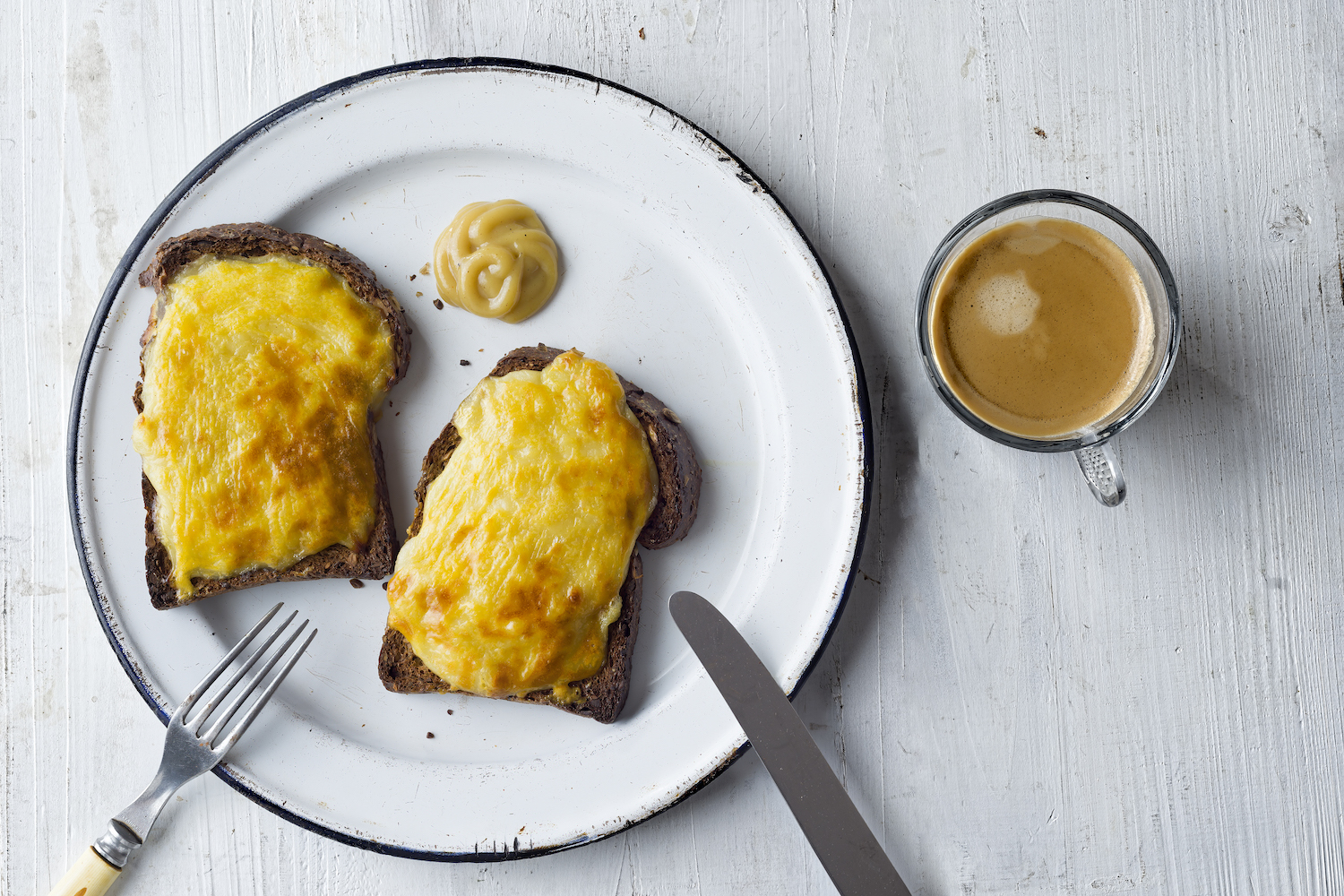 welsh rarebit cheese sauce toast on a white plate next to a cup of coffee