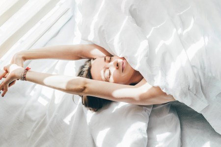 top view of a woman sleeping under a white duvet on a sunny morning