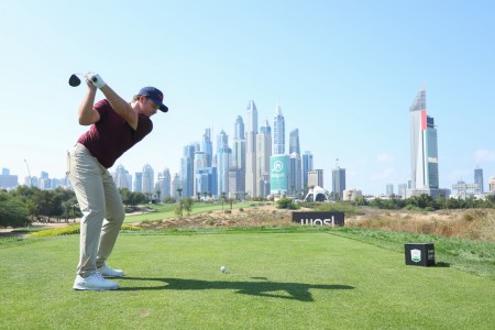 Golfer Eddie Pepperell tees off at a golf tournament with the Dubai skyline in front of him